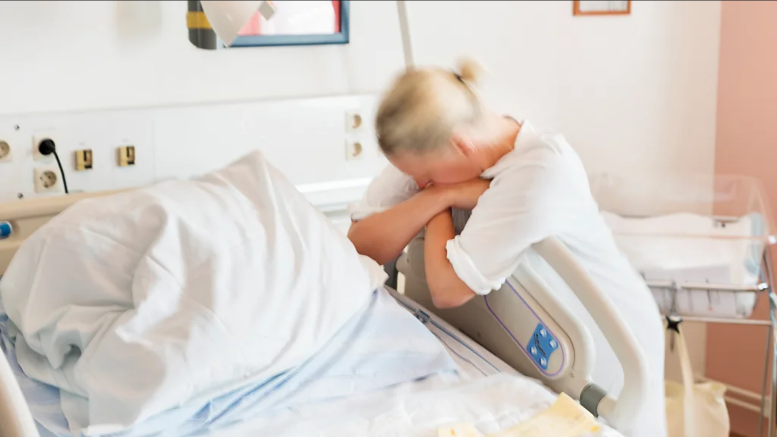 Žene nisu predodređene da rađaju ležeći na leđima, pa zašto to rade 3 Žena pored bolničkog kreveta na nogama, grli dršku od kreveta, glava joj je na rukama