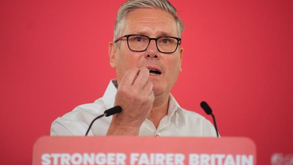 Starmer za govornicom ispred koje je tabla na kojoj je slogan: 'Jača i poštenija Britanija'