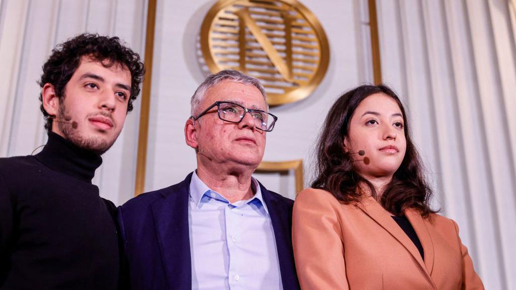 Tagi Rahmani, Ali Rahmani i Kijana Rahmani poziraju za fotografiju tokom konferencije za novinare u Nobelovom institutu. Zlatni Nobelov logo je vidljiv u pozadini. Sva troje nose male mikrofonske štitnike.