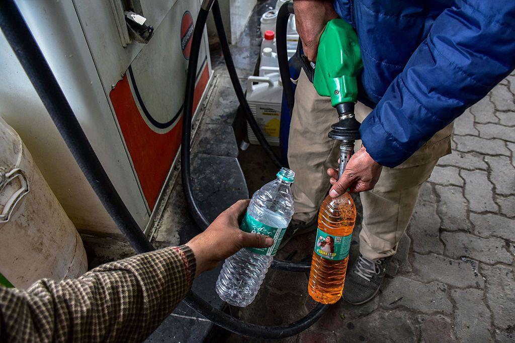 Radnik na benzinskoj pumpi u plavoj perjanoj jakni sipa gorivo u plastičnu flašu, dok je u kadru vidljiva i druga ruka koja drži praznu flašu.