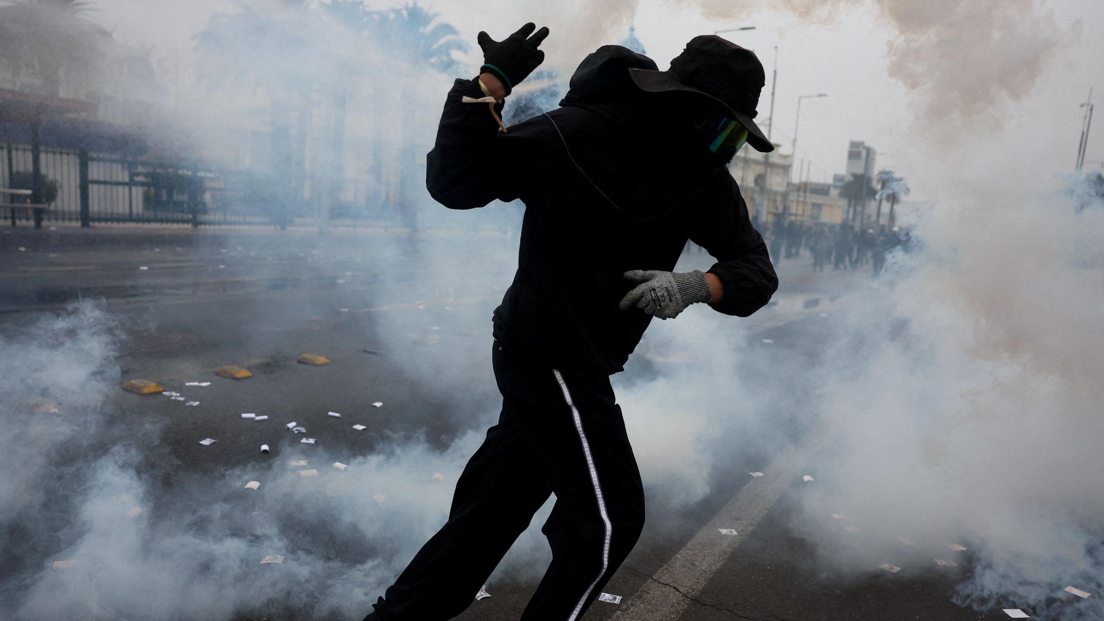 Prvi maj širom sveta: Protesti, suzavac i rejv 2 muškarac u crnoj dukserici i trenerci trči kroz oblak suzavca, nosi masku i šešir preko lica, na rukama rukavice