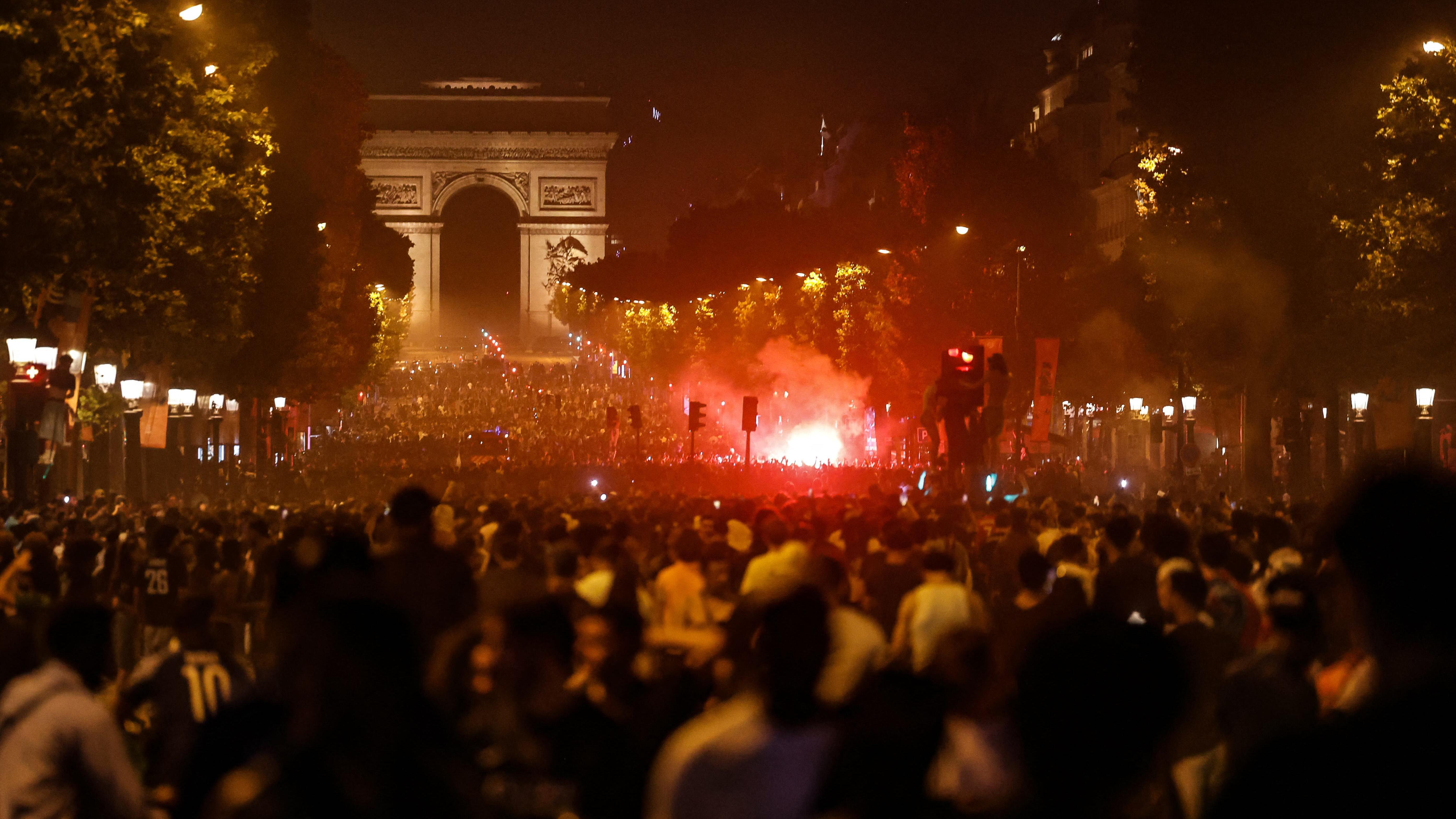 Haos u Parizu: Stotine uhapšenih i povređenih tokom proslave pobede PSŽ-a u Ligi šampiona 2 Bustling crowds swamp Avenue des Champs-Élysées, lit up by a ball of red flares along the landmark mall. The Arc de Triomphe can be seen at the end of the avenue.