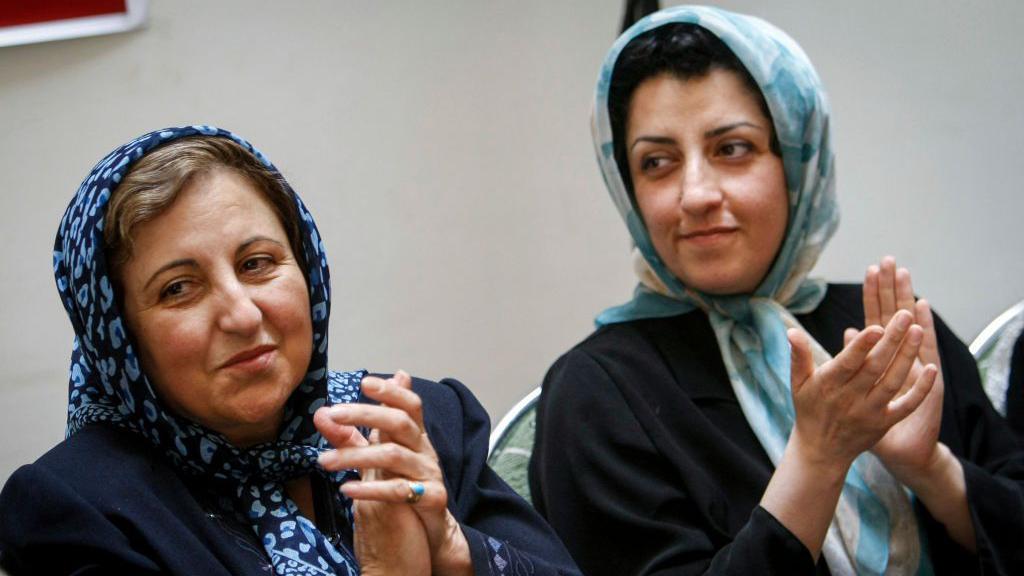 Širin Ebadi i Narges Mohamadi aplaudiraju tokom konferencije za novinare. Ebadi nosi tamnoplavu maramu sa šarom, na kojoj se vidi deo kose, dok Mohamadi nosi svetloplavu maramu sa šarom, na kojoj se vidi deo njene kose, i crni sako.