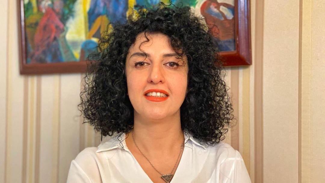 Narges Mohamadi se osmehuje na ovoj nedatiranoj slici sa brošure. Ima crnu kovrdžavu kosu i nosi belu košulju, ogrlicu u obliku trougla i crveni karmin.