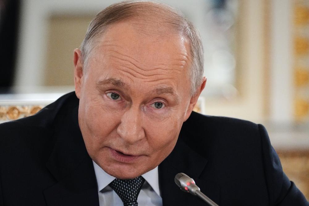 Putinu tamnom odelu sedi za stolom i govori