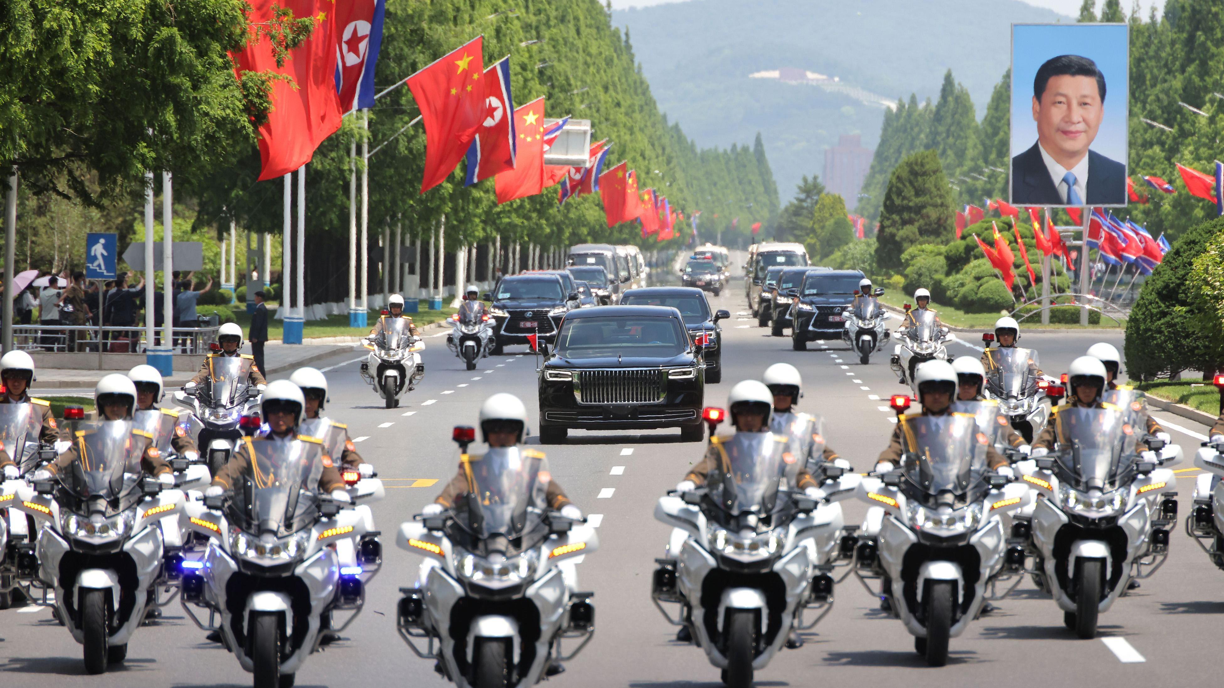 Baloni i zimzeleno drvo: Kineski i severnokorejski lideri obećavaju jače veze 4 Desetine motociklista ispred nekolicine crnih automobila na jednoj od bandera slika kinekog predsednika Sija Đinpinga