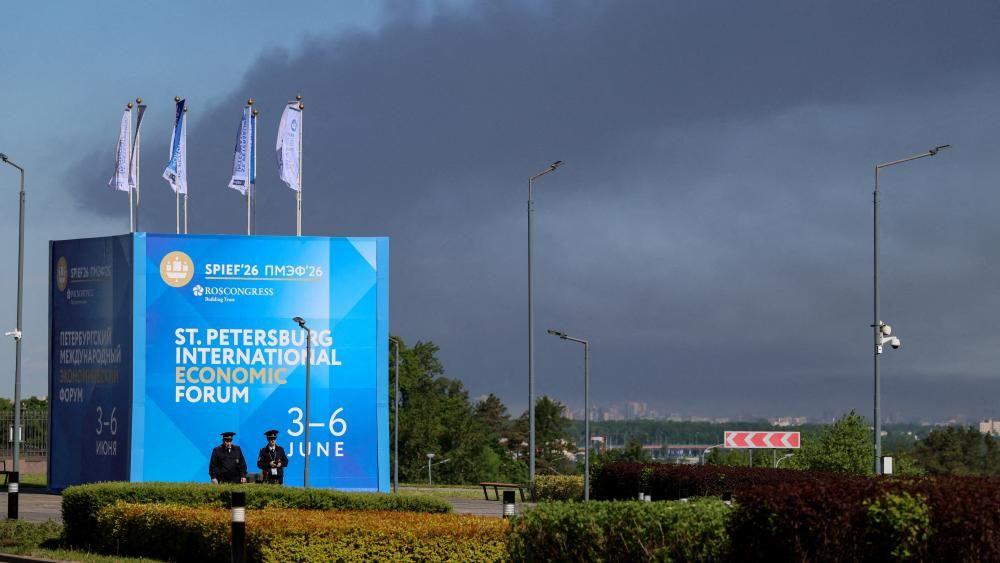 Ruski ekonomski forum u senci napada dronovima na Sankt Peterburg: BBC urednik 4 Policijajci stoje ispred transparenta i zastava sa logom Sanktpeterburškog međunarodnog ekonomskog foruma (SPIEF) dok u pozadini kulja gust dim posle pogotka ukrajinskih dronova u infrastrukturu
