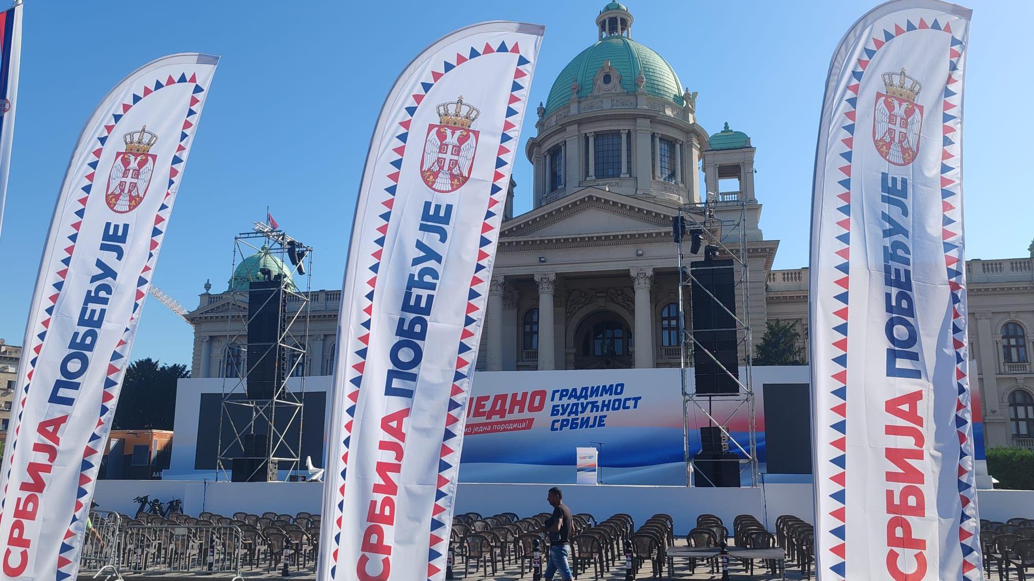 Čovek prolazi ispred stolica i skupštine, okolo su zastave za miting vladajuće stranke u Srbiji