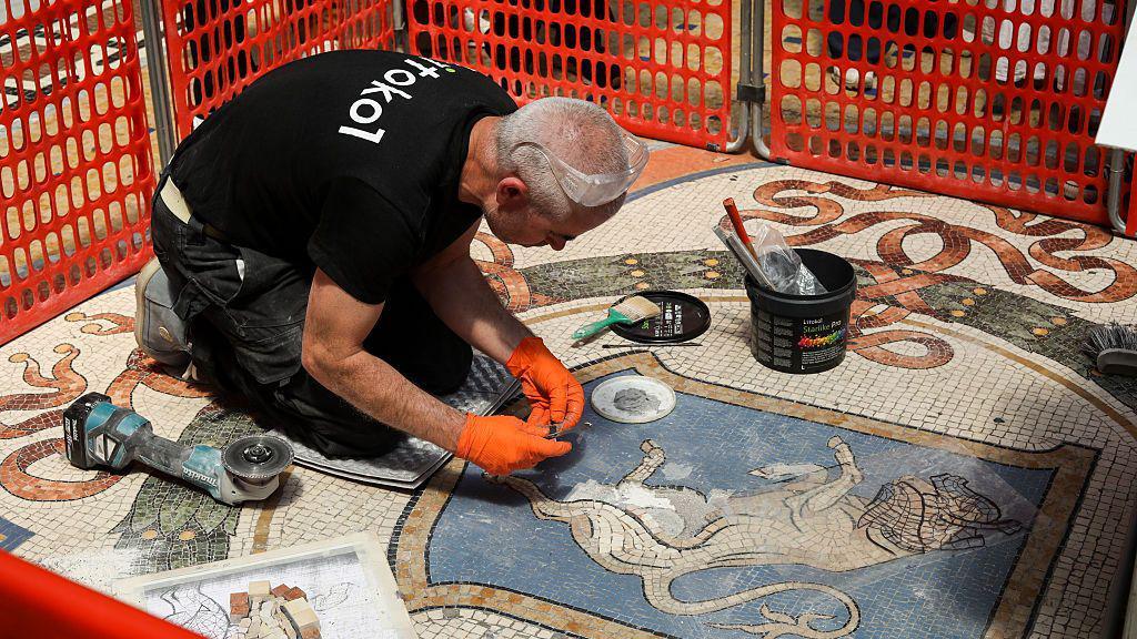Šta ste uradili sa testistima? Italijani u čudu zbog restauracije čuvenog mozaika 1 Restaurator kleči ispred mozaika bika. Na sebi ima narandžaste rukavice i crnu majicu, dok je oko njega postavljena narandžasta zaštitna ograda