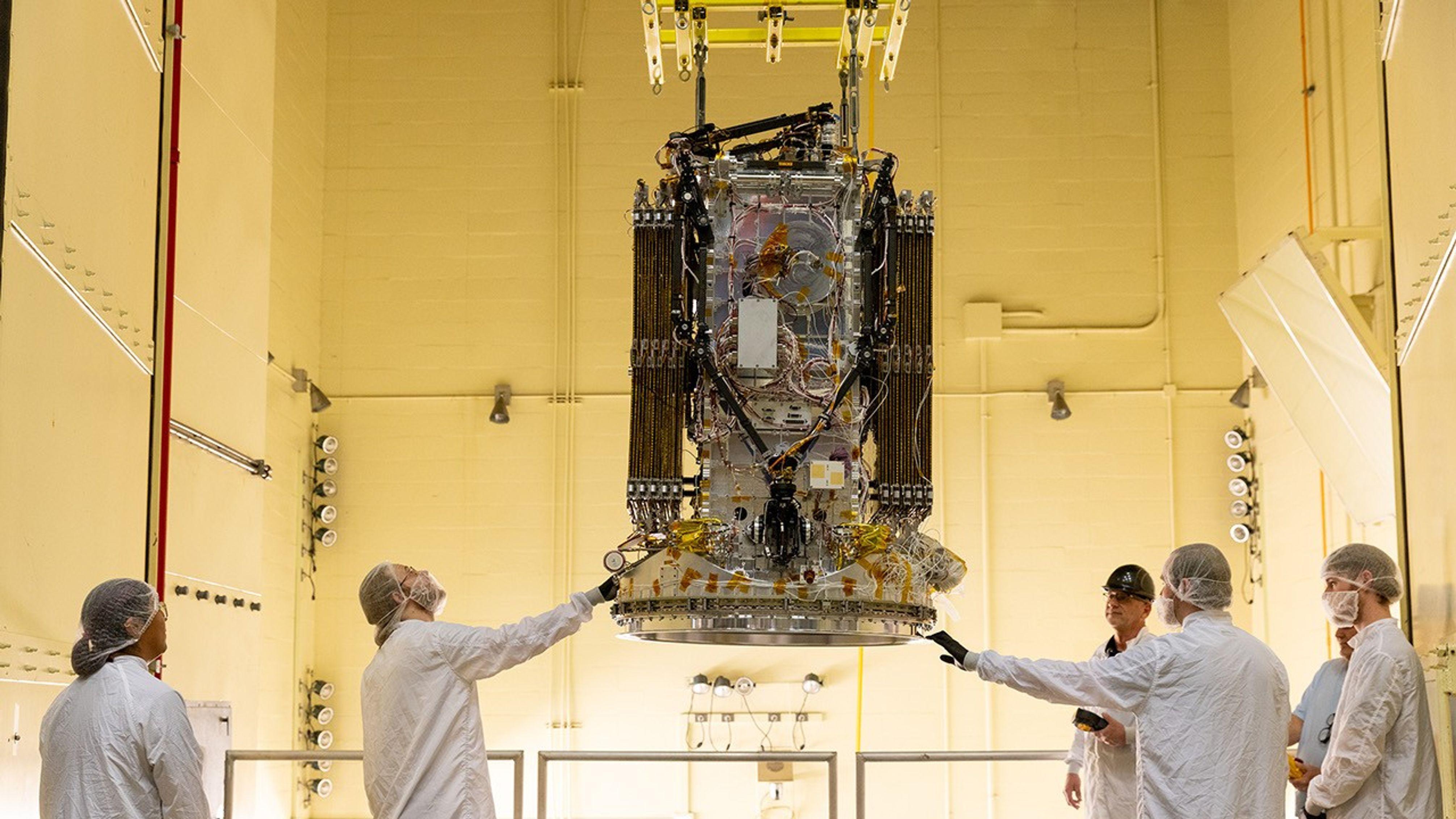 NASA šalje robota po teleskop Svift da ne padne na Zemlju 2 U jarko žutoj testnoj komori, šest inženjera u belim laboratorijskim mantilima i mrežicama za kosu stoji oko velike svemirske letelice okačene o plafon